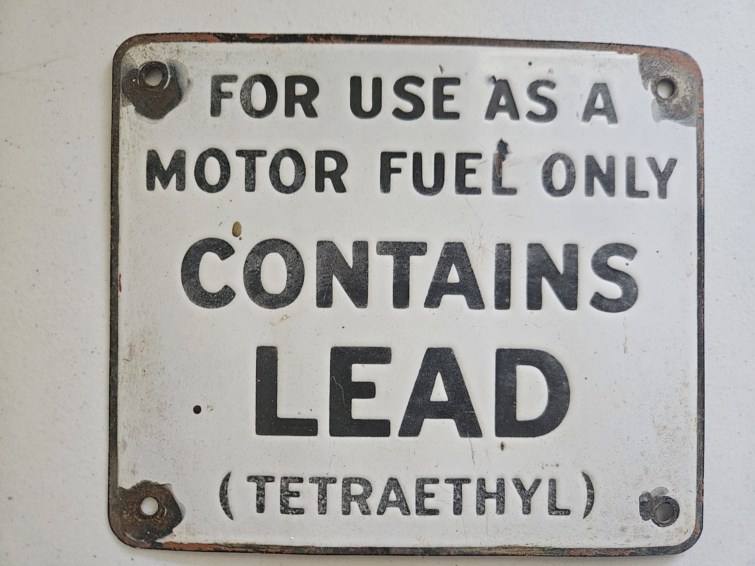 Weathered metal warning sign stating that the container is for use as motor fuel only and contains lead